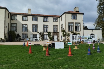 Un espace extérieur avec une table dressée près d'un étang, des arbres et un groupe de personnes au loin.
