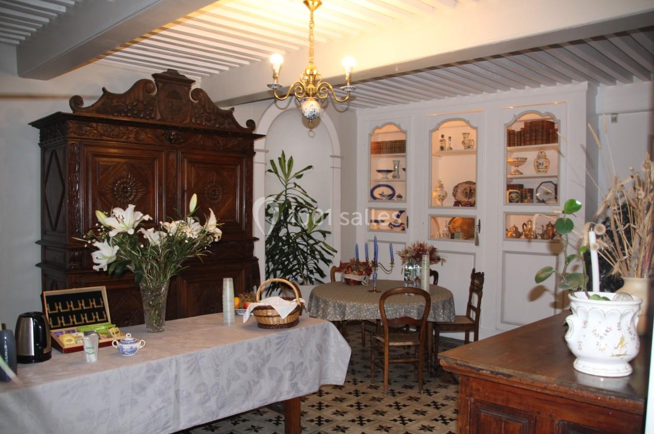 Salle à manger rustique avec meubles en bois, table dressée, fleurs, vaisselier et carrelage ancien au sol.