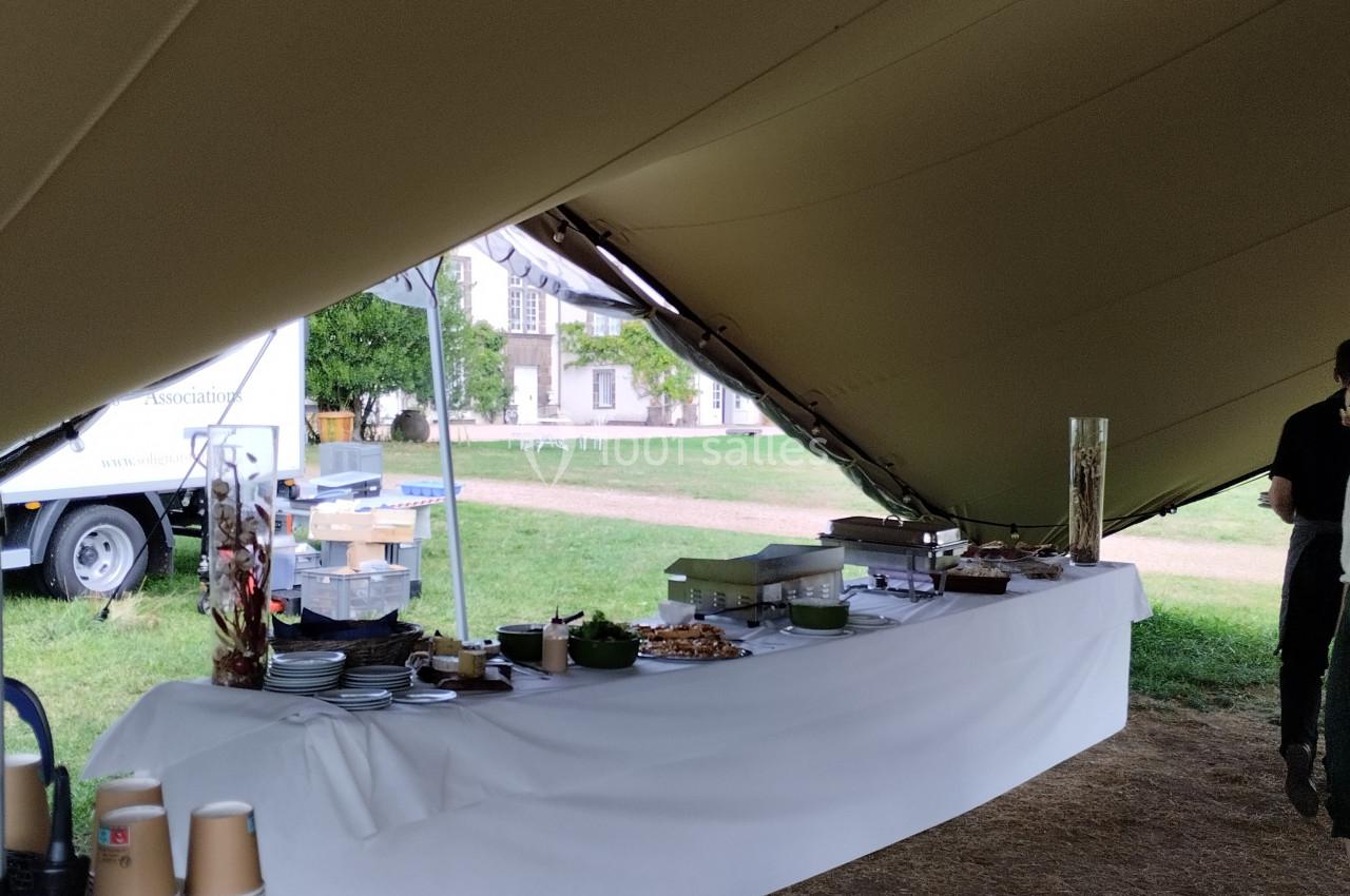 Table dressée sous une tente avec vaisselle, plats et boissons pour un buffet en extérieur.