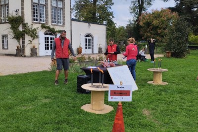 Un espace extérieur avec une table dressée près d'un étang, des arbres et un groupe de personnes au loin.