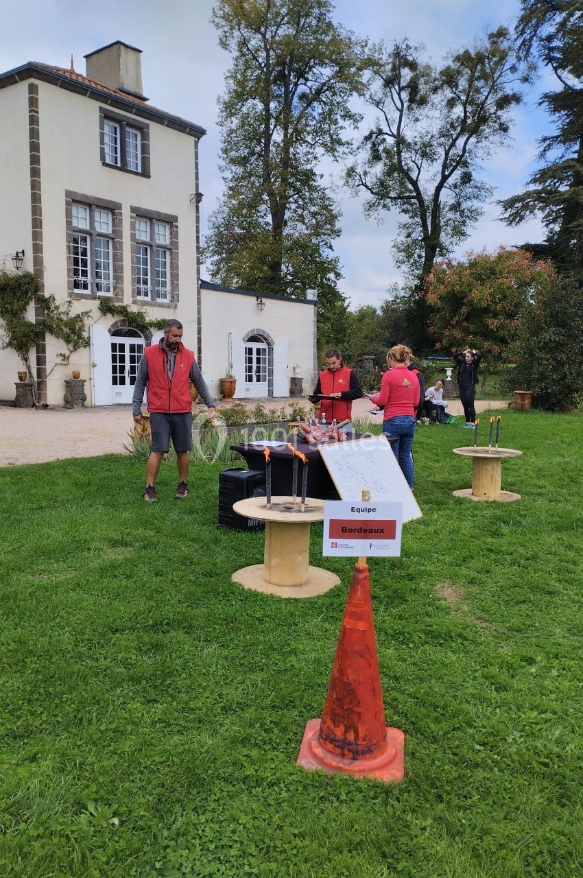 Personnes disposant des objets sur une pelouse devant un bâtiment, avec des tables et un panneau ’Équipe Bordeaux’.