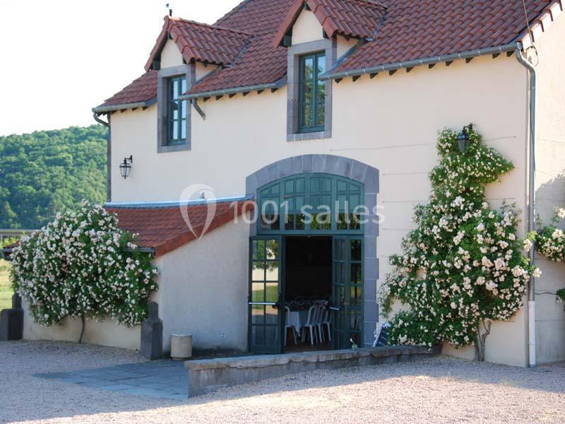 Façade d'une maison avec toit en tuiles, grandes fenêtres et rosiers grimpants fleuris de chaque côté.