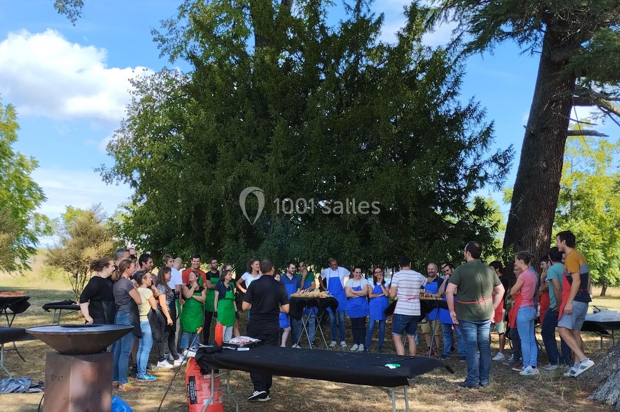 Un groupe de personnes rassemblées en plein air près de tables et d'arbres, participant à une activité collective.