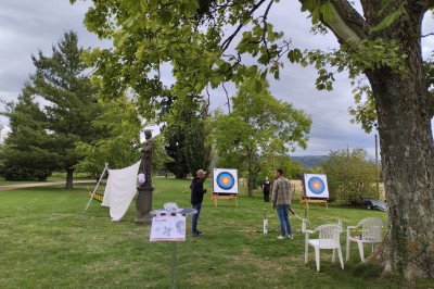 Un espace extérieur avec une table dressée près d'un étang, des arbres et un groupe de personnes au loin.
