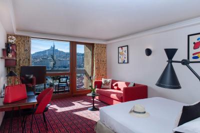 Une femme de dos sur une terrasse, face au Vieux-Port de Marseille, avec une table dressée pour le petit-déjeuner.