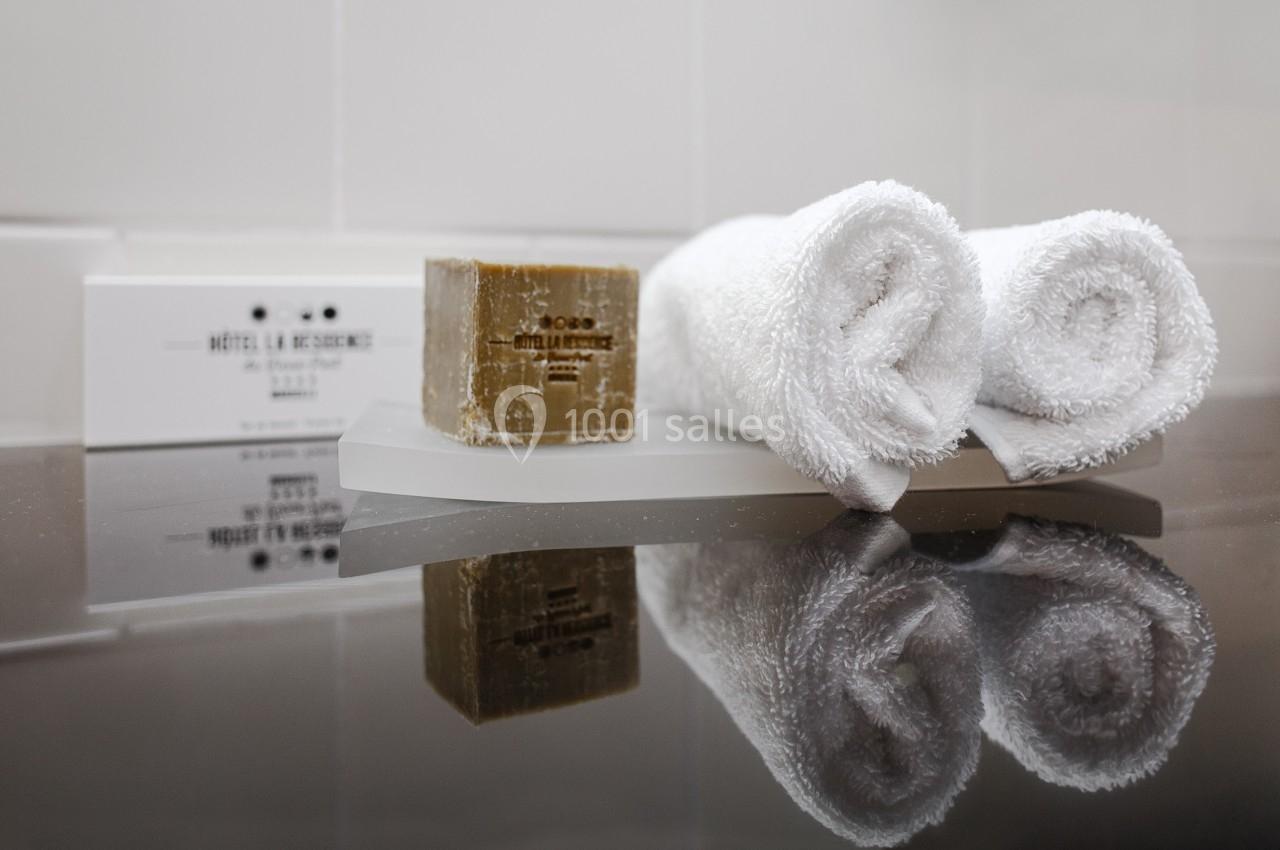 Deux serviettes blanches roulées, un savon et des articles de toilette disposés sur un plateau dans une salle de bain.