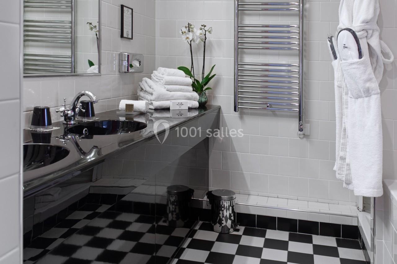 Salle de bain moderne avec carrelage noir et blanc, lavabo, miroir, porte-serviettes chauffant et orchidée blanche.