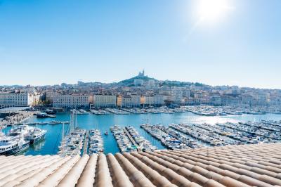 Une femme de dos sur une terrasse, face au Vieux-Port de Marseille, avec une table dressée pour le petit-déjeuner.