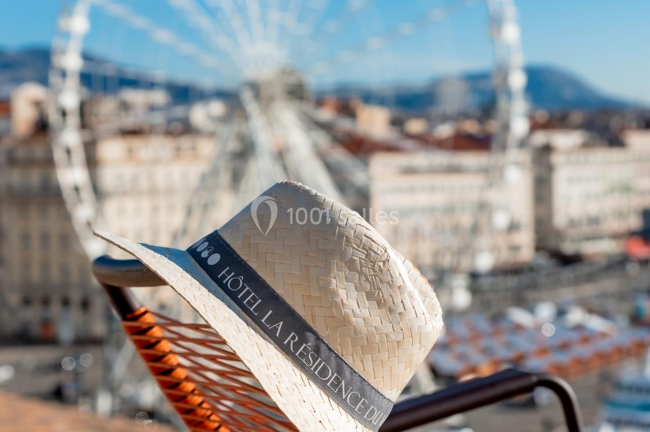 Chapeau en paille marqué ’Hôtel La Résidence’ posé sur une chaise, avec une grande roue en arrière-plan.