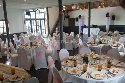 Table de réception décorée avec nappes blanches, serviettes vertes pliées, chaises ornées de nœuds verts et centre de table…