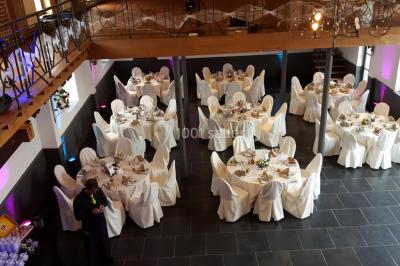 Table de réception décorée avec nappes blanches, serviettes vertes pliées, chaises ornées de nœuds verts et centre de table…