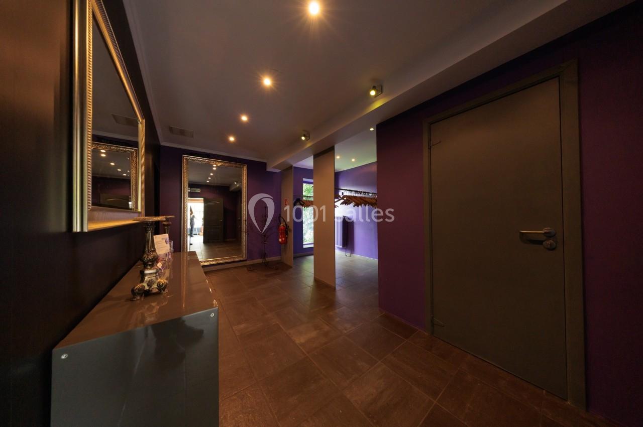 Couloir moderne avec murs violets, sol en carrelage foncé, éclairage encastré et porte fermée à droite.