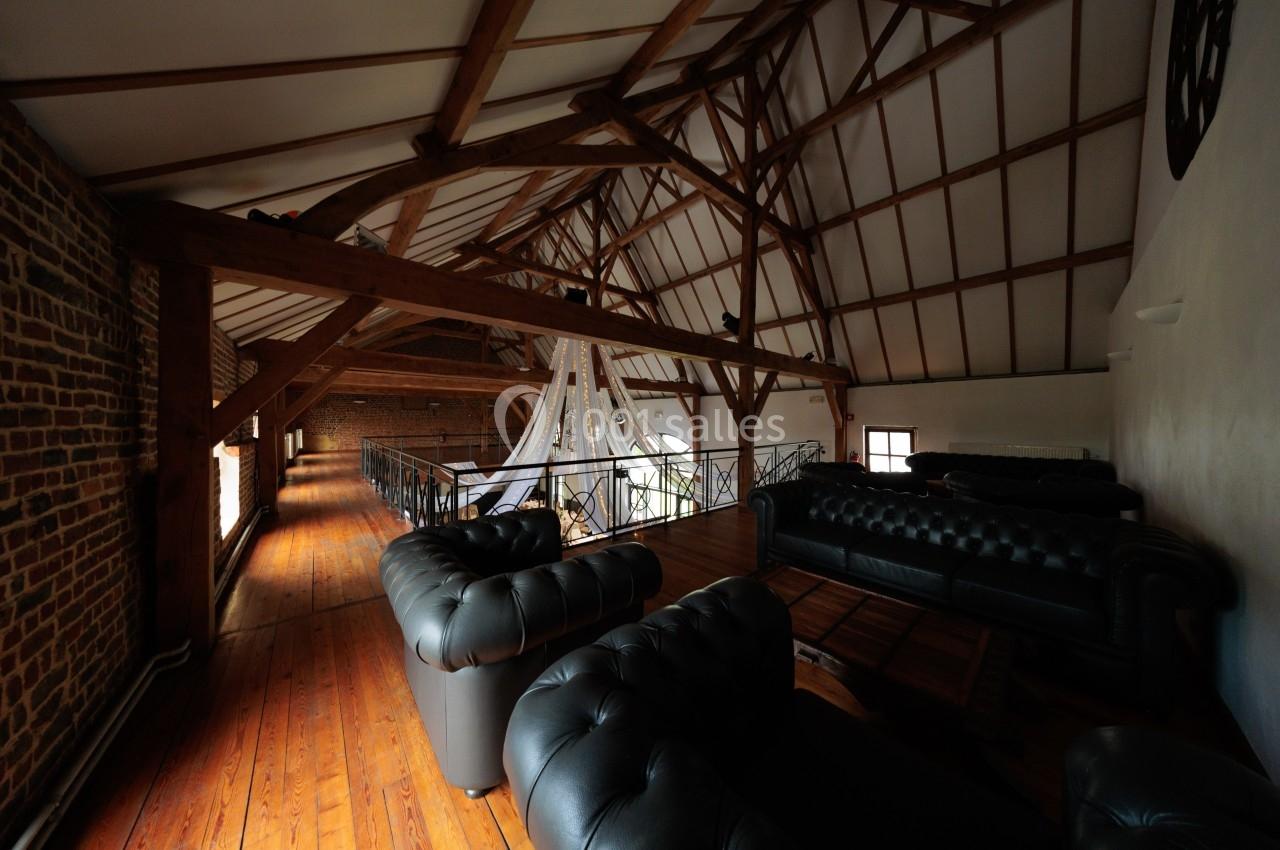 Intérieur d'un loft avec poutres apparentes, canapés en cuir noir et mezzanine en bois.