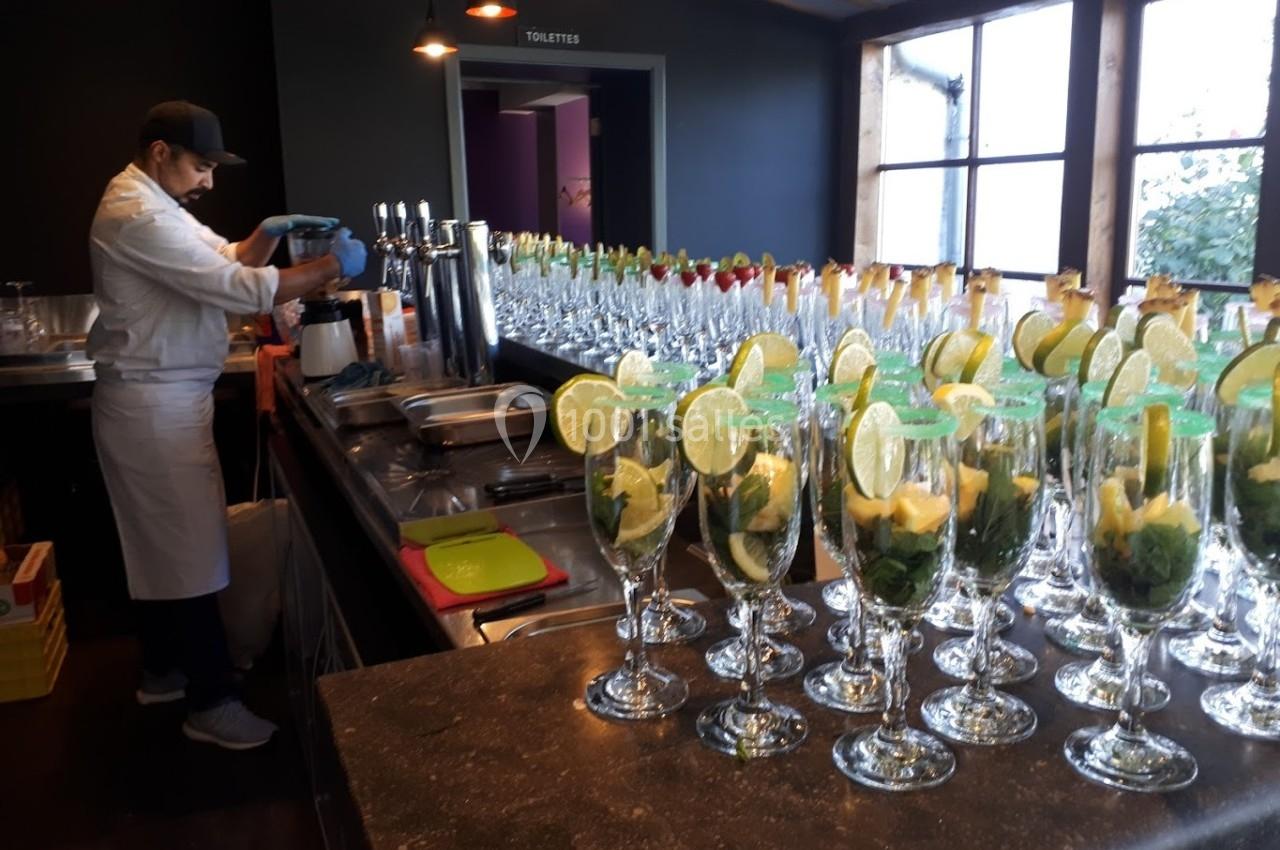 Un barman prépare des cocktails dans une cuisine avec des verres garnis de menthe, citron vert et ananas alignés sur le…