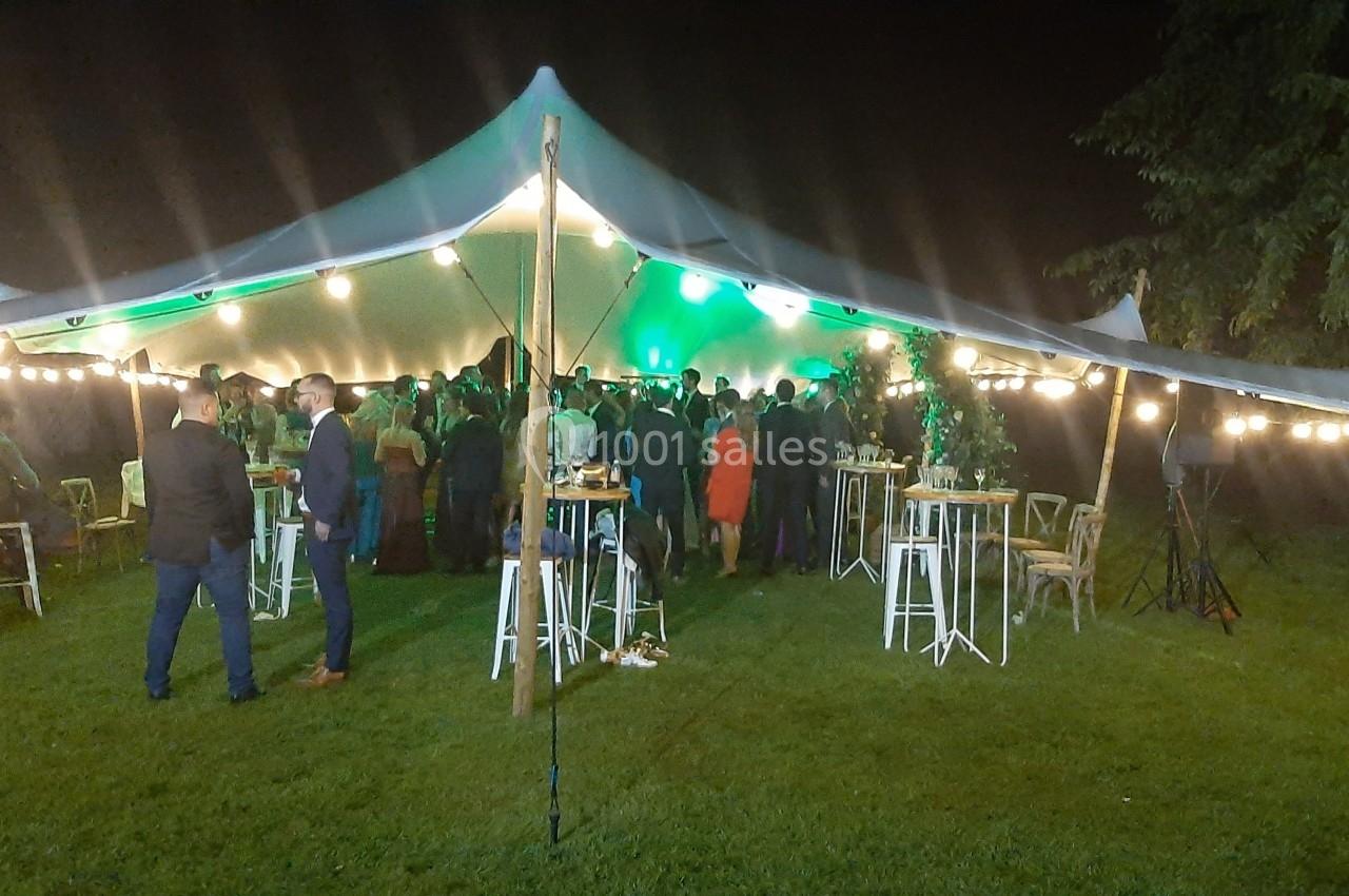 Tente éclairée accueillant un événement nocturne avec des invités debout autour de tables hautes sur une pelouse.