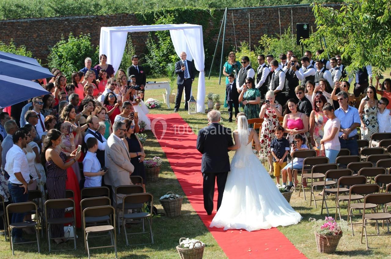 Un mariage en plein air avec une mariée marchant sur un tapis rouge, accompagnée d'un homme, devant des invités assis.