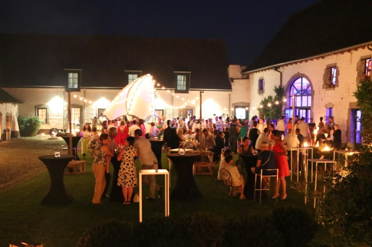 Groupe de personnes rassemblées en soirée dans une cour éclairée par des guirlandes lumineuses.
