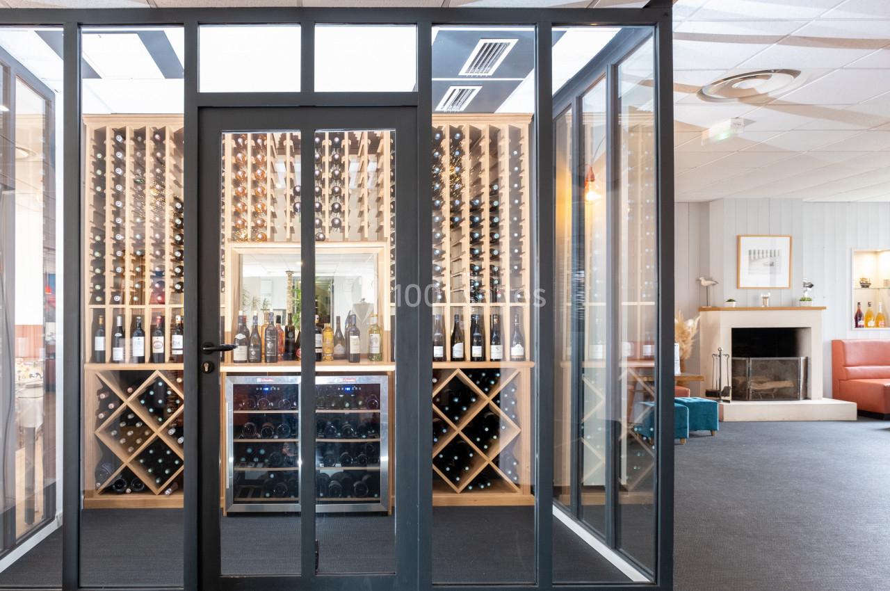 Cave à vin vitrée avec étagères remplies de bouteilles, située dans un espace intérieur lumineux et moderne.