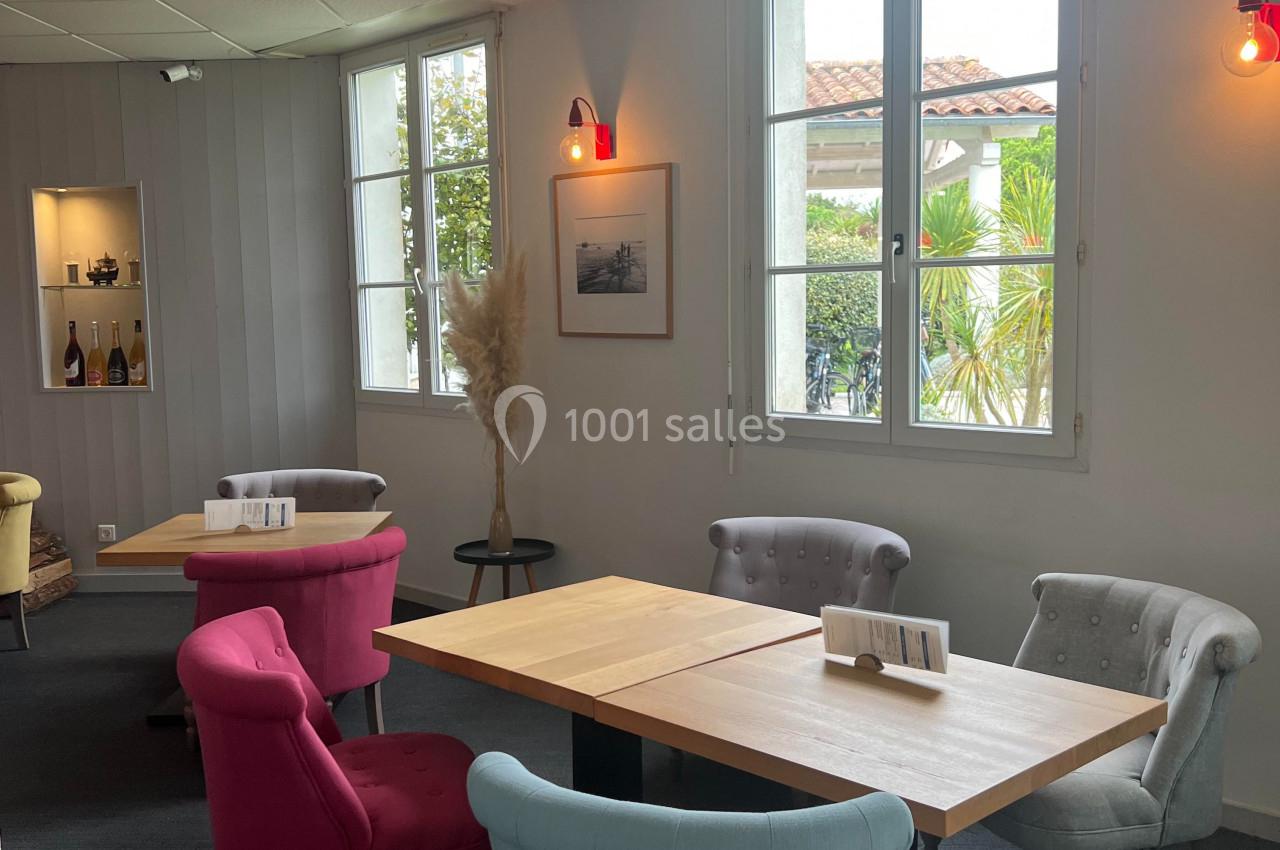 Salle lumineuse avec tables en bois, chaises colorées et décoration sobre, vue sur l'extérieur par de grandes fenêtres.