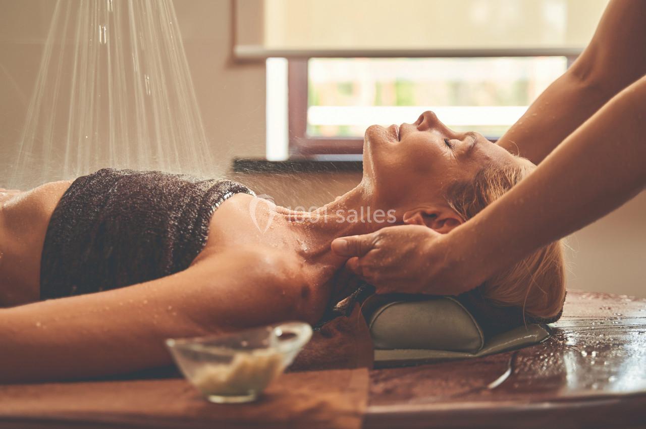 Femme allongée recevant un massage sous une douche d'eau, dans un cadre lumineux et relaxant.