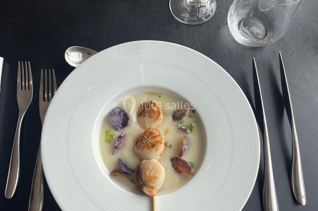 Assiette de noix de Saint-Jacques grillées sur purée, garnie de chips violettes, servie avec des couverts élégants.