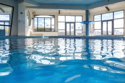 Quatre chevaux blancs galopent sur une plage au bord de l'eau, sous un ciel de coucher de soleil.