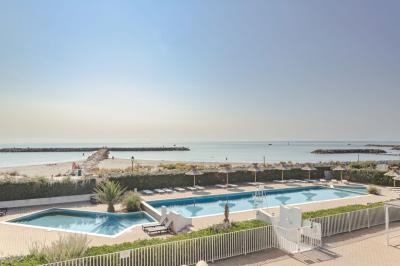 Quatre chevaux blancs galopent sur une plage au bord de l'eau, sous un ciel de coucher de soleil.