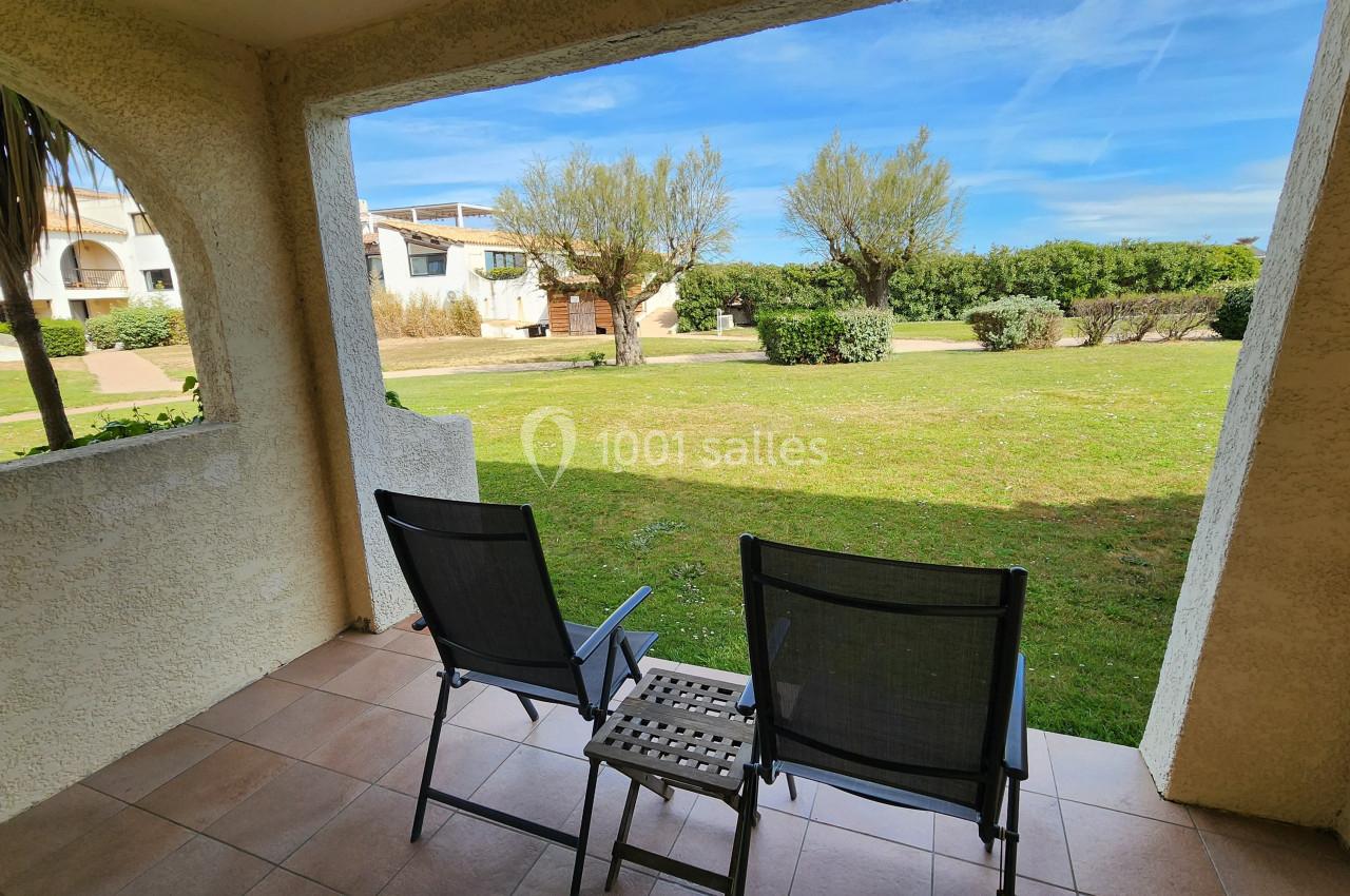 Deux chaises noires sur une terrasse donnant sur un jardin verdoyant avec des arbres et un ciel dégagé.
