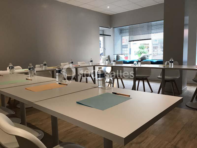 Salle de réunion lumineuse avec tables blanches disposées en U, chaises modernes et fournitures de bureau.