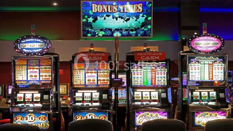 Quatre machines à sous alignées dans un casino, avec des écrans lumineux affichant des jeux et des jackpots.
