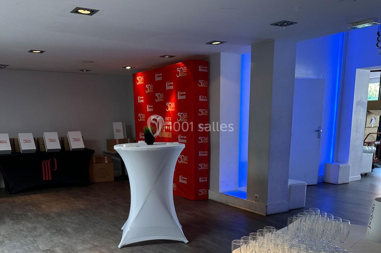 Salle avec un présentoir, des cartons empilés, une table haute décorée et un fond rouge marqué ’50 ans’.