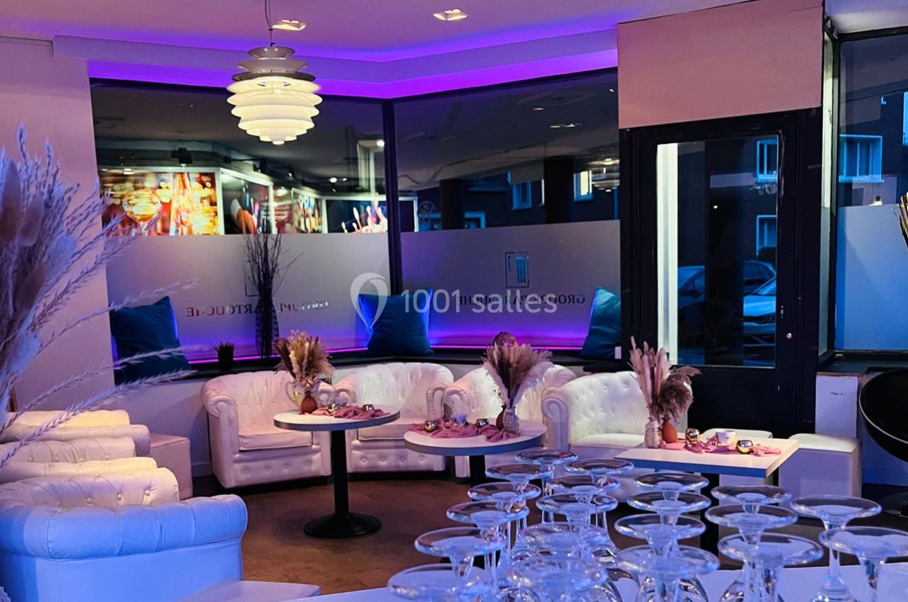 Salon moderne avec canapés blancs, tables basses décorées et éclairage violet, donnant sur une grande baie vitrée.