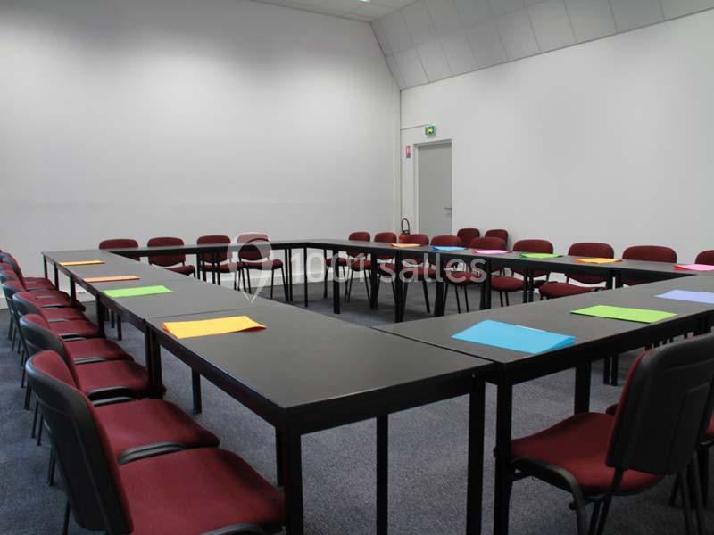 Salle de réunion avec des tables disposées en U, des chaises rouges et des feuilles colorées posées sur les tables.