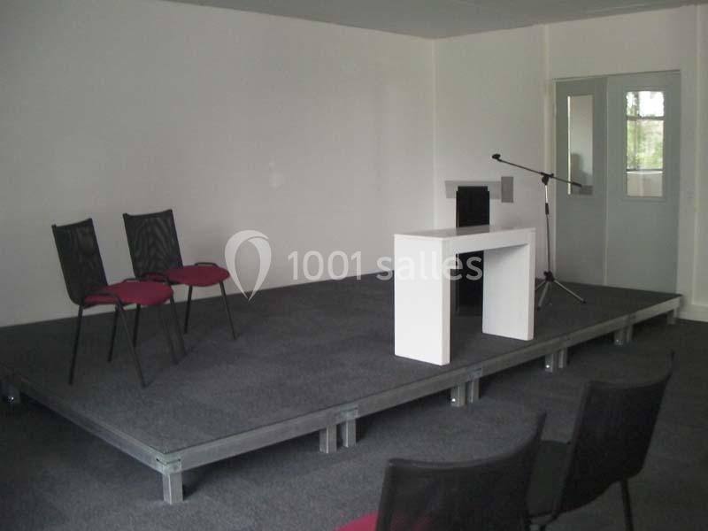 Estrade avec deux chaises, un pupitre blanc et un micro sur pied dans une salle aux murs blancs.