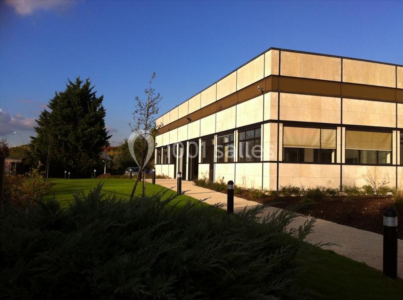 Bâtiment moderne avec façade beige, grandes fenêtres et jardin paysager sous un ciel dégagé.