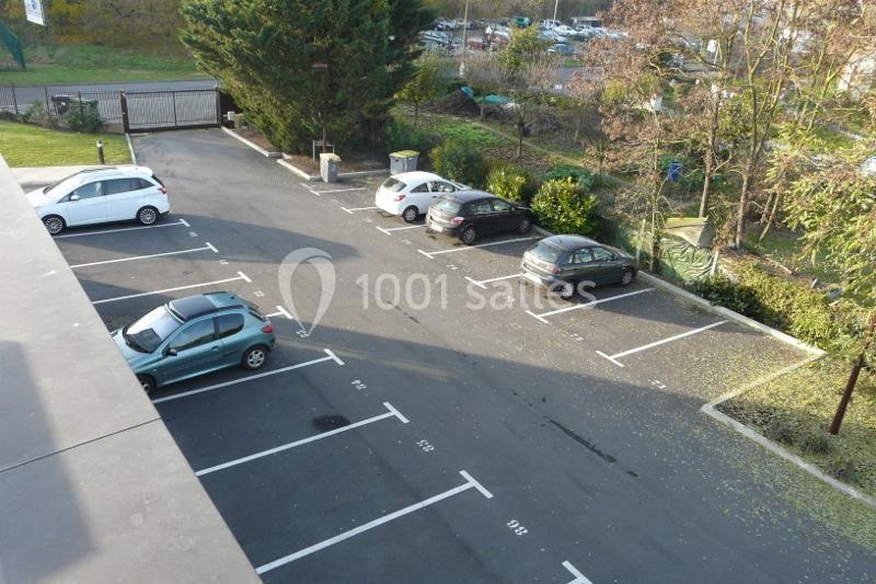 Vue aérienne d'un parking extérieur partiellement occupé, entouré de végétation et d'une clôture.