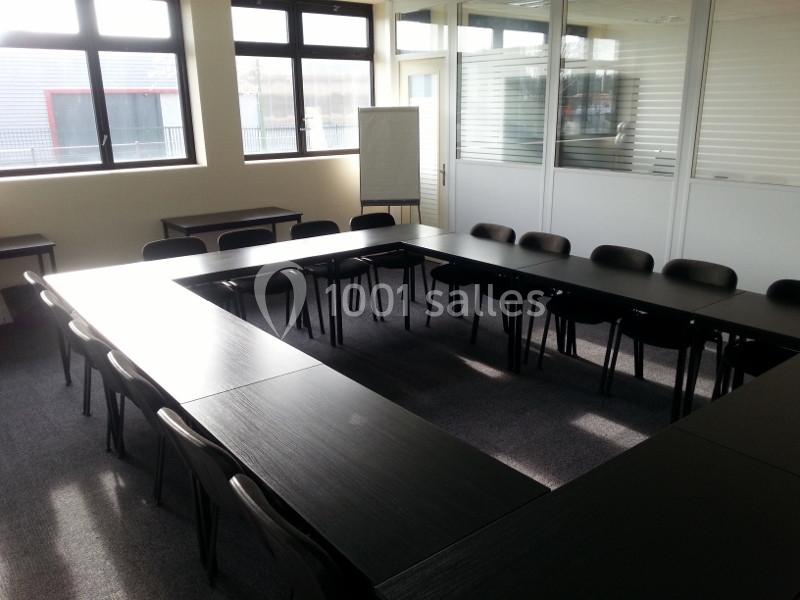 Salle de réunion lumineuse avec des tables disposées en U et des chaises noires autour.