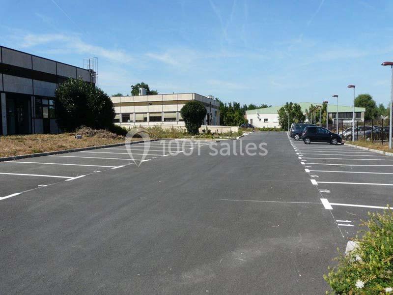 Parking vide avec marquages au sol, entouré de bâtiments et de végétation sous un ciel dégagé.