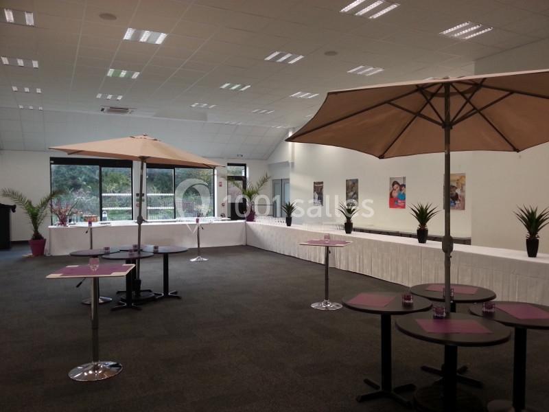 Salle lumineuse aménagée avec des tables, des parasols et des plantes, prête pour un événement ou une réception.