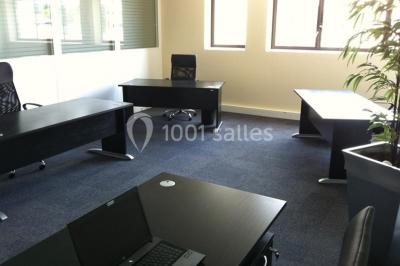 Bureau lumineux avec plusieurs postes de travail équipés de meubles noirs, un ordinateur portable visible au premier plan.