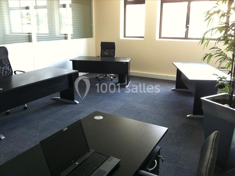 Bureau lumineux avec plusieurs postes de travail équipés de meubles noirs, un ordinateur portable visible au premier plan.