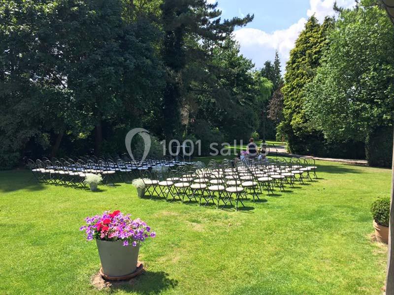 Chaises alignées en extérieur sur une pelouse, entourées d'arbres, avec un pot de fleurs au premier plan.