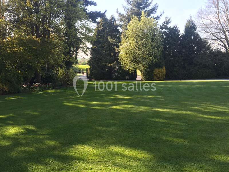 Pelouse verte bien entretenue entourée d'arbres et de buissons sous un ciel dégagé.
