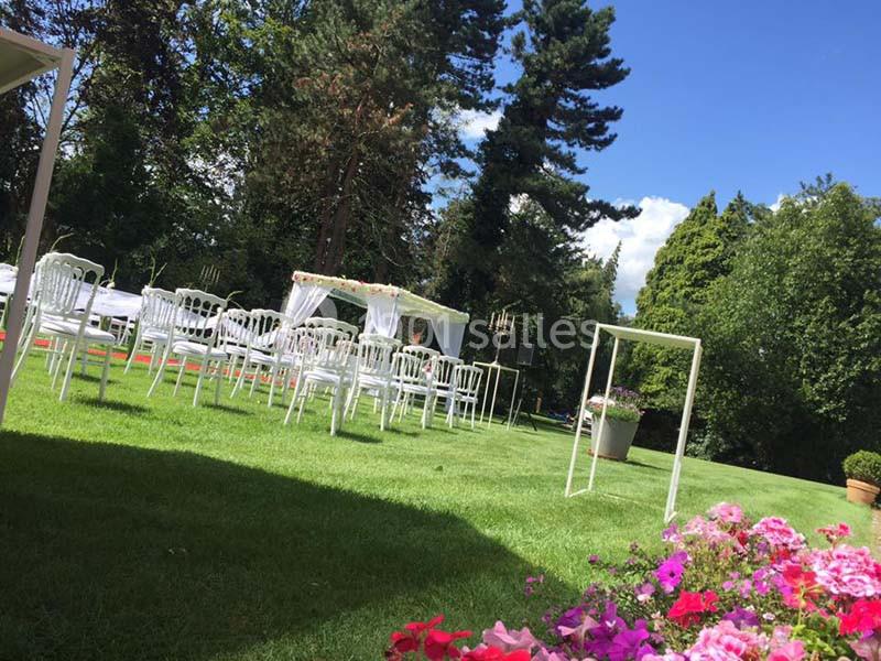 Chaises blanches disposées en extérieur sur une pelouse, avec une arche décorée pour une cérémonie en plein air.