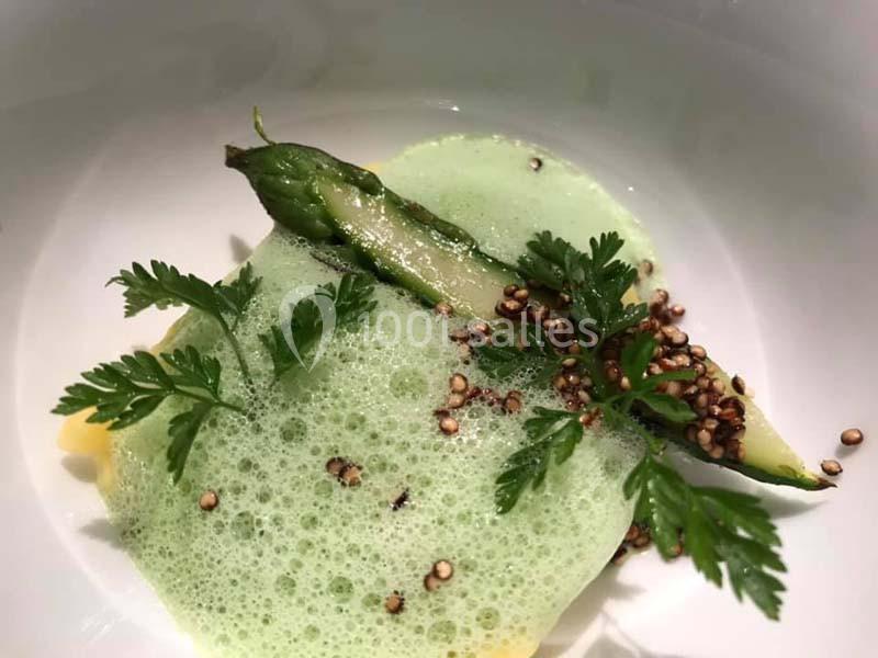 Asperge verte avec mousse verte, graines toastées et feuilles de cerfeuil dans une assiette blanche.