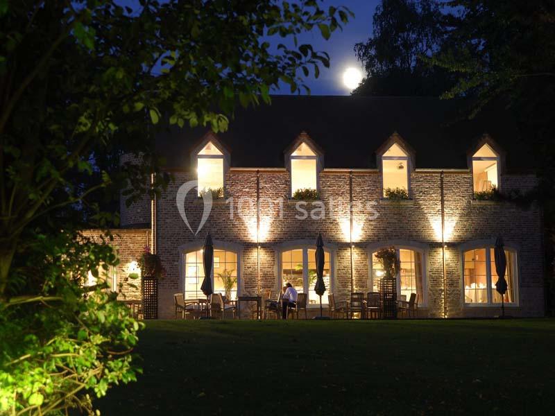 Façade d'une maison en briques éclairée la nuit, avec des fenêtres illuminées et une terrasse aménagée.