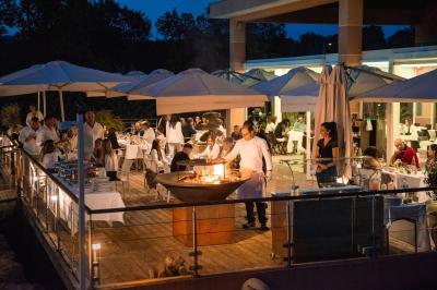 Salle de réception lumineuse avec tables dressées, grandes compositions florales et vue sur une terrasse arborée.