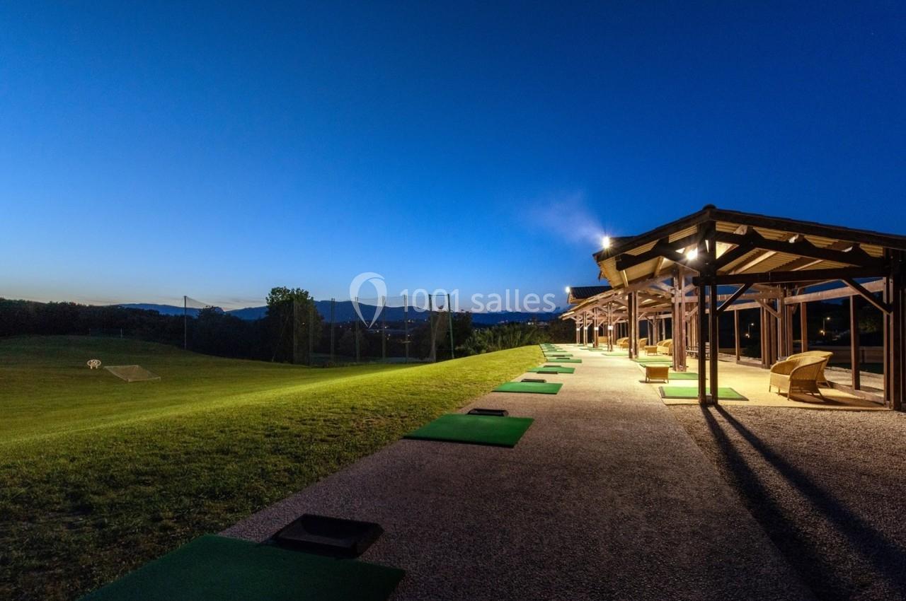 Terrain de practice de golf en soirée, avec des tapis de frappe alignés et un éclairage sous un ciel dégagé.