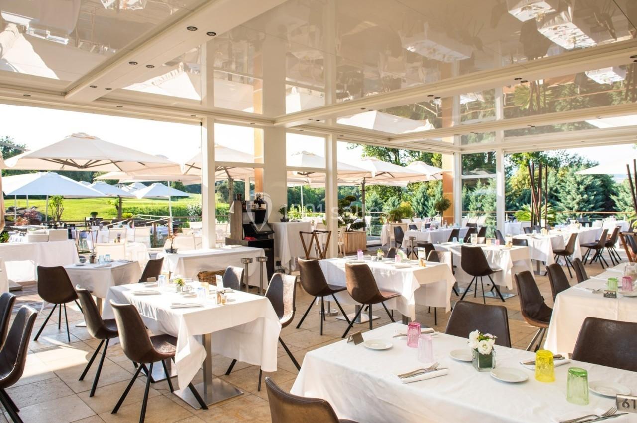 Salle de restaurant lumineuse avec tables dressées, grandes baies vitrées et terrasse extérieure avec parasols.