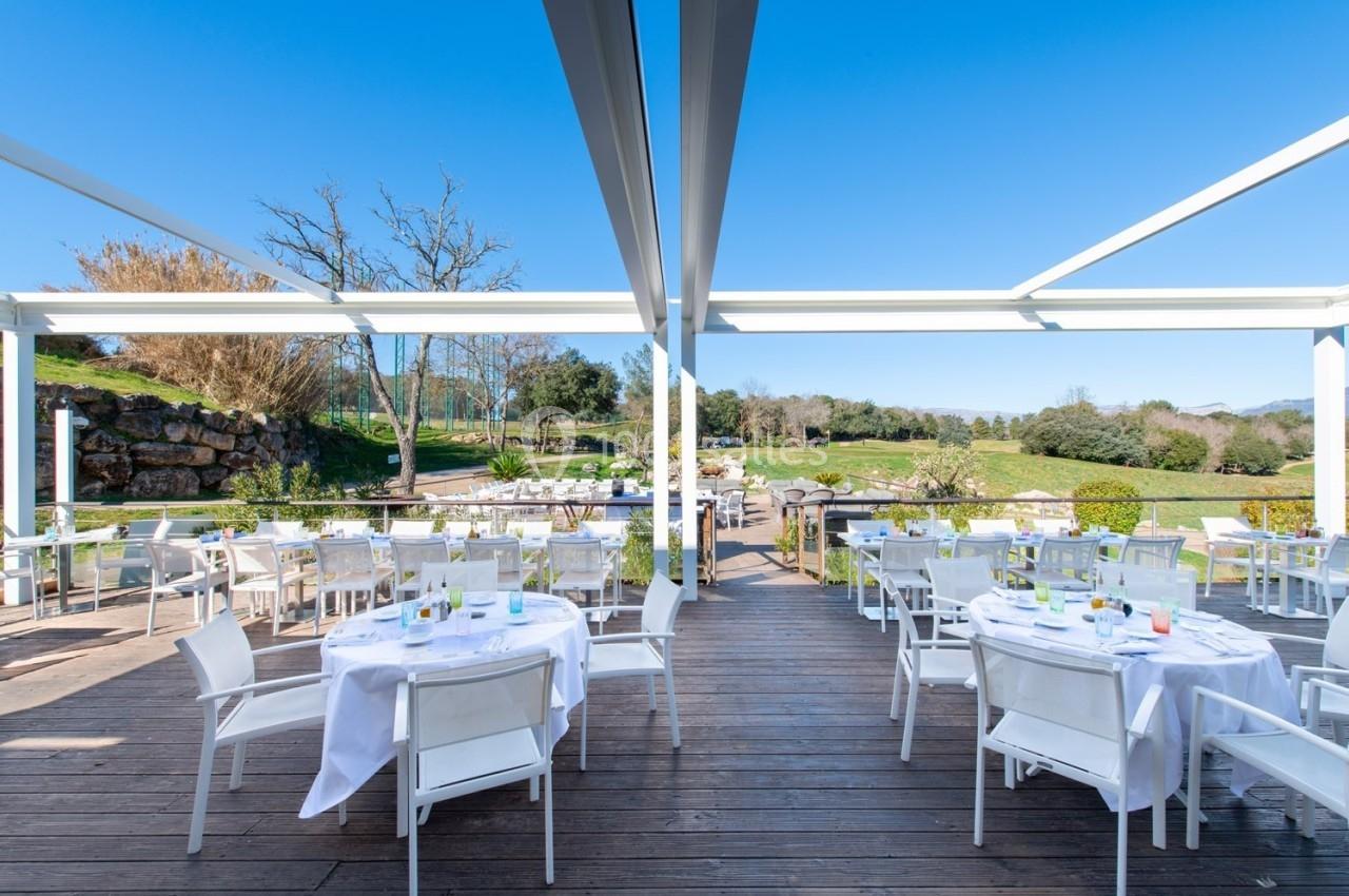 Terrasse ensoleillée avec tables dressées sous une pergola, offrant une vue sur un jardin verdoyant et un ciel dégagé.